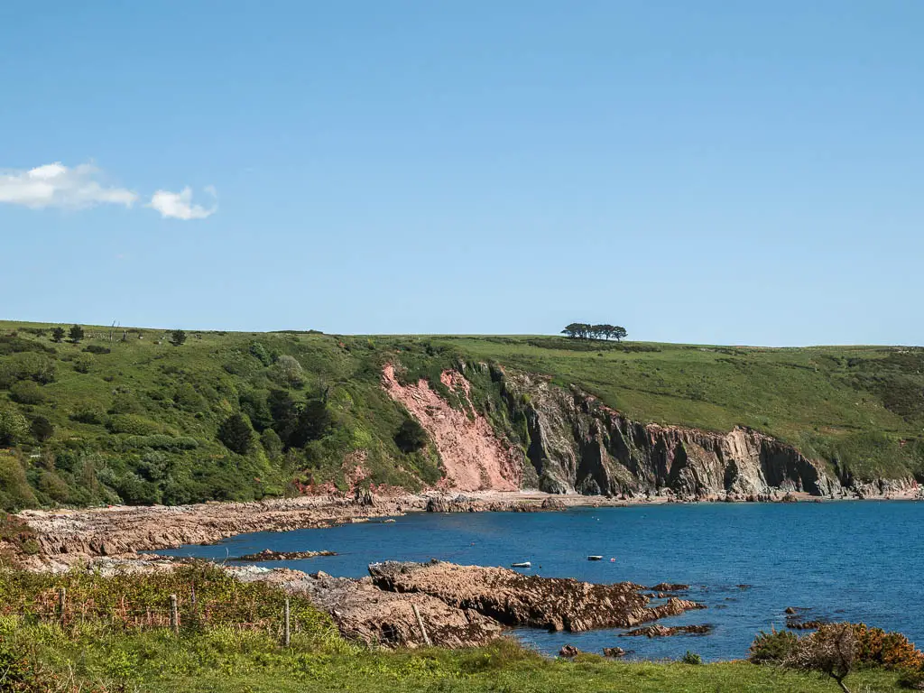 Looking across the grass to the blue sea and cliffs covered in grass on the other side, on the circular Noss Mayo walk.
