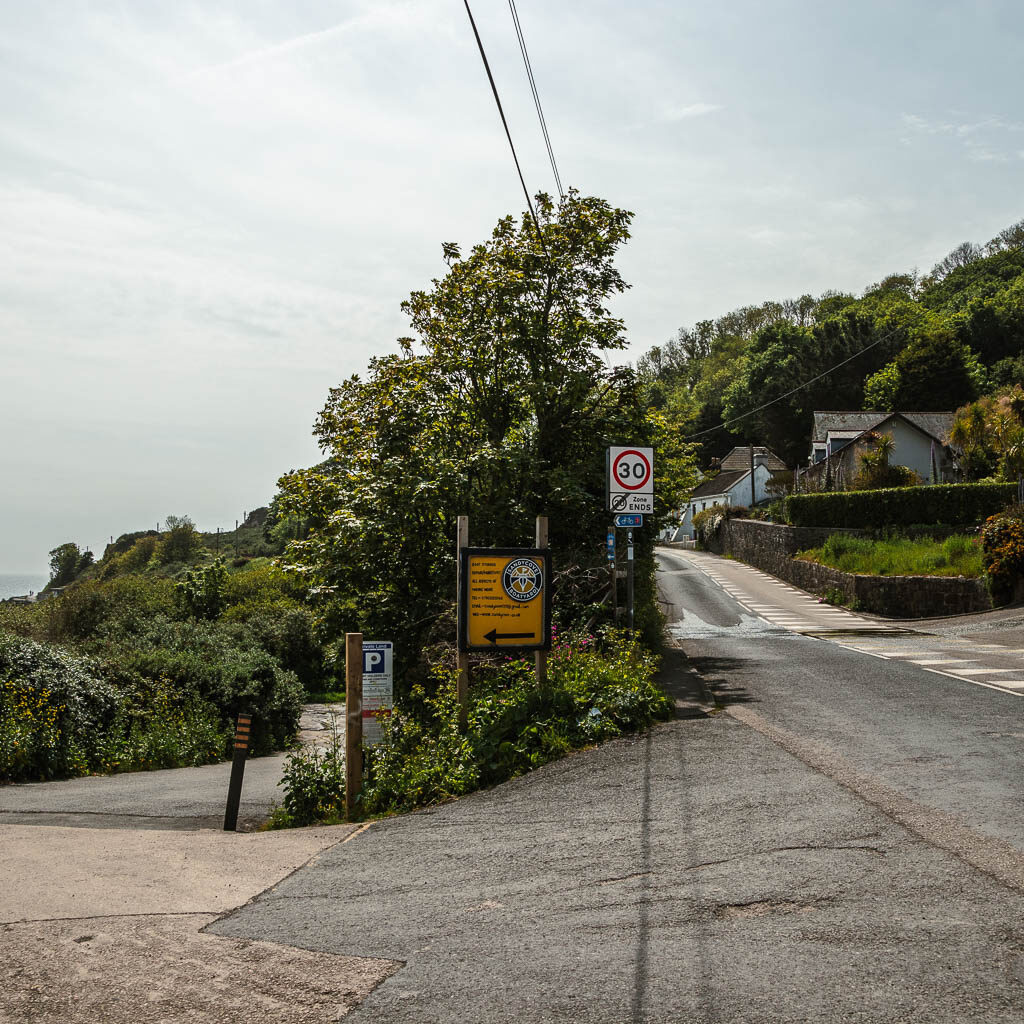 A road junction, with the right one going straight and up hill, and the left one staying level and leading to some trees. 