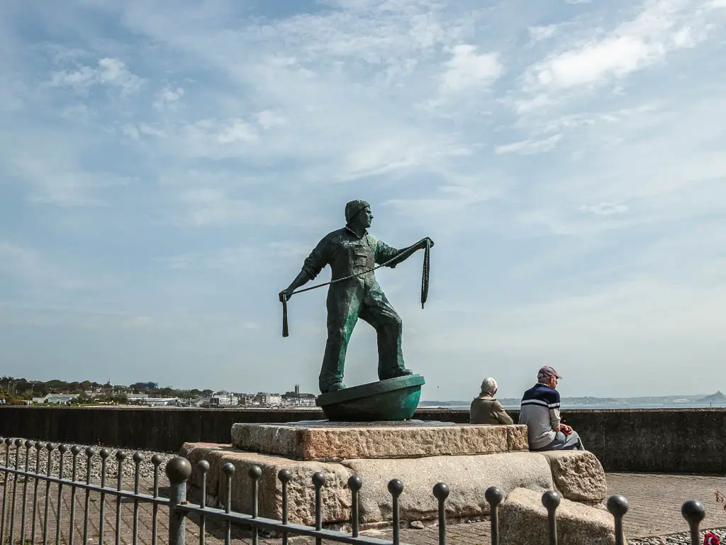 A statue of a man on slabs of rock. There are people sitting on the rock.