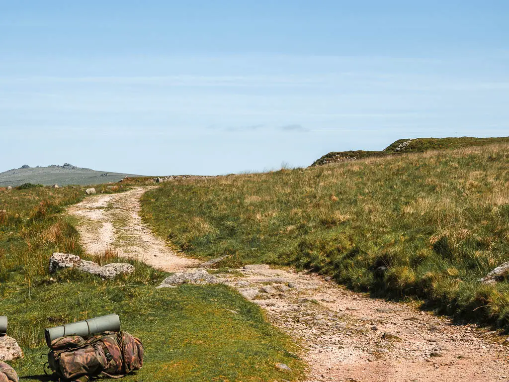The rocky offshoot of the Princetown Railway path through the grass, on the walk to King's Tor. There is an army backpack on the left on the grass.