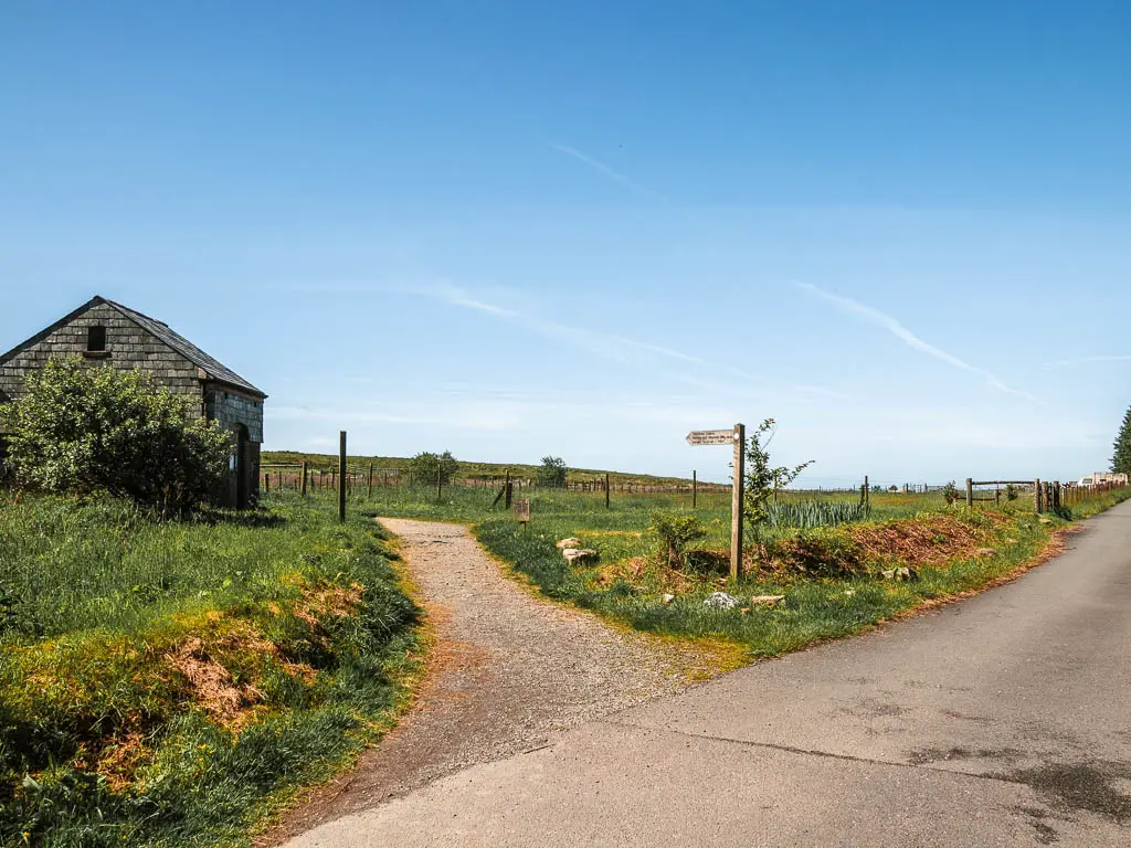 A trail leading off the road, at the start of the Princetown Railway walk to King's tor. The trail runs through the grass, and there is a shed on the left side of the trail.
