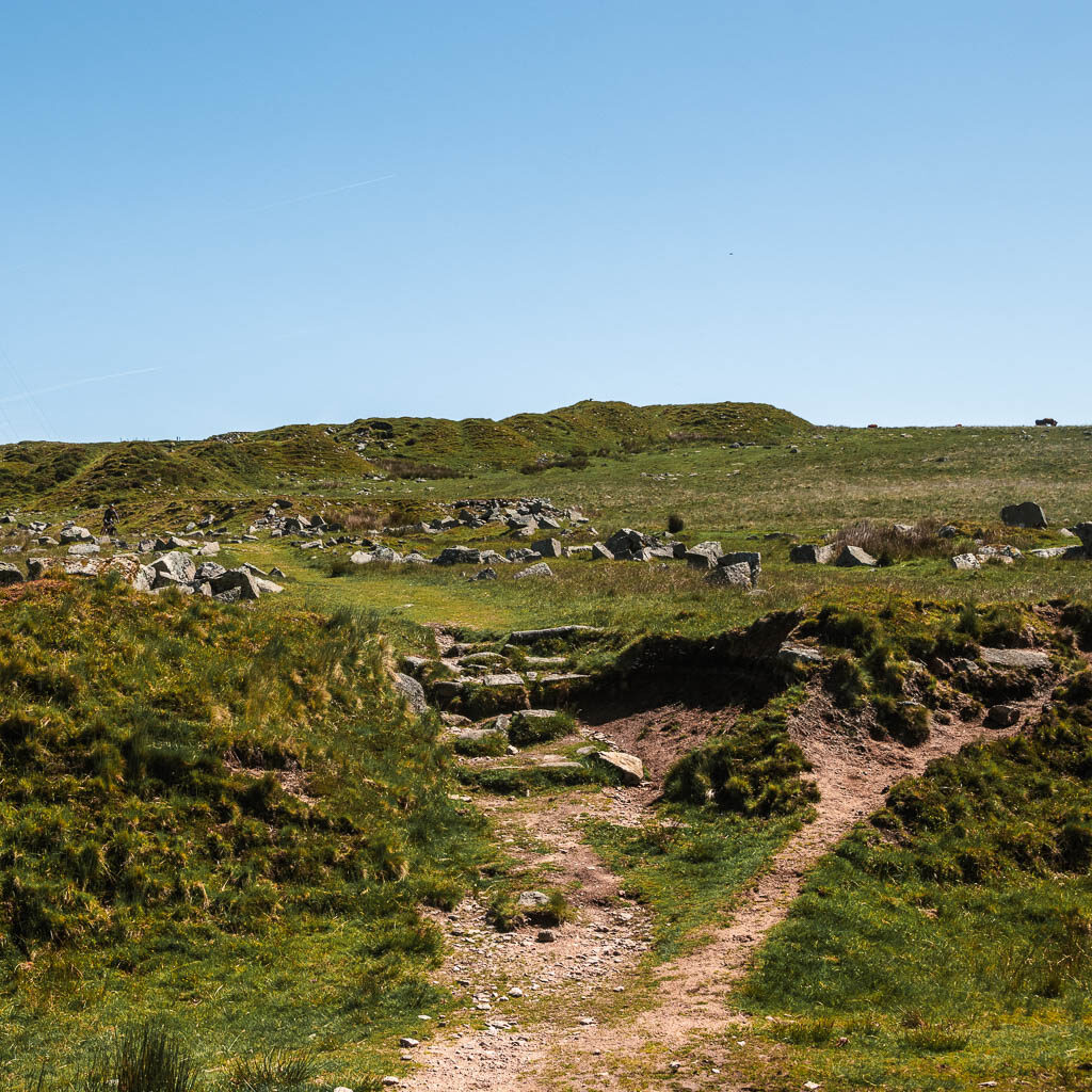 A rocky trail leading up towards a green hill ahead.