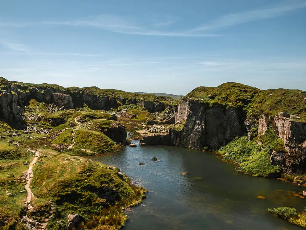 Looking down into Foggintor Quarry, on the circular walk from Princetown along the old railway. The water in the quarry is calm and surrounded by a grass and moss covered ground, and enclosed by rock cliffs.