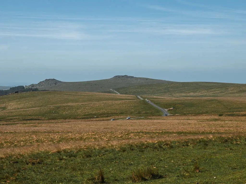 Looking across the moor towards some hills in the distance on the Princetown Railway walk. There is a road running across the moor.