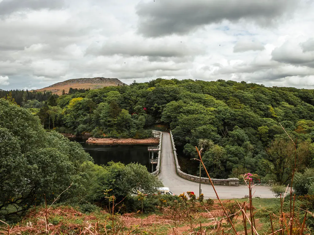 Looking down to the Burrator reservoir Bridge on the Sheepstor circular walk. The bridge is surround by lots of trees and the top of Sheepstor is visible in the distance.