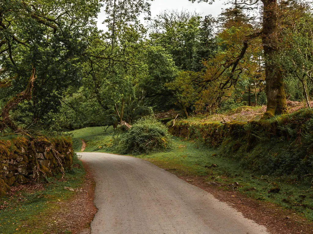 A road curving ahead to the left, with a moss covered wall on the right, and stone wall on the left.