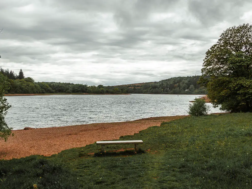 A stone bench on the green, leading to the reservoir with a view to lots of trees in the distance. 