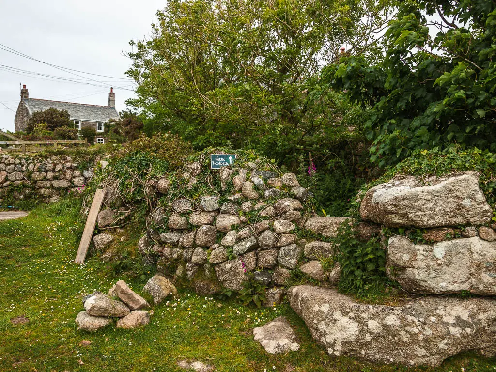 A rugged stone wall, with stone steps leading over it on the walk back to St Ives from Zennor. There is a cute house half visible past the wall on the left.