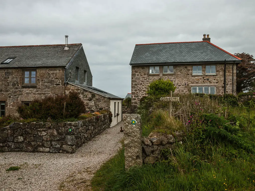 Stone hoses, with a gap though the middle for the coast path. There is a wooden coast path sign pointing to the gap.