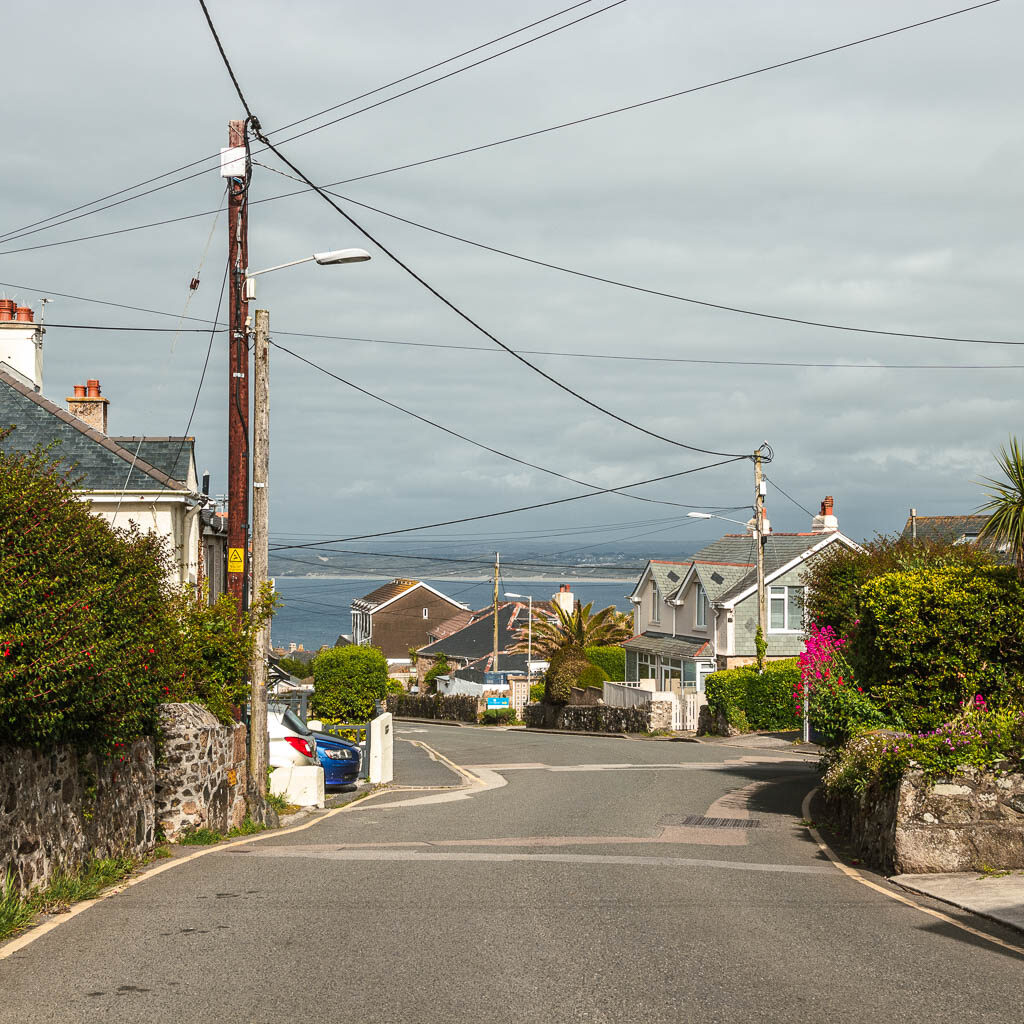 the main road leading down towards some hoses, and the sea in the distance. There are lots of electricity  wires up high.