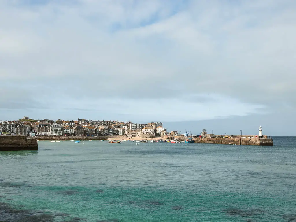 Looking across the sea to the bay of St Ives ahead, at the end of the coastal walk to Zennor. The sea is pale blue and turquoise. There are lots of houses on the other side of the bay.