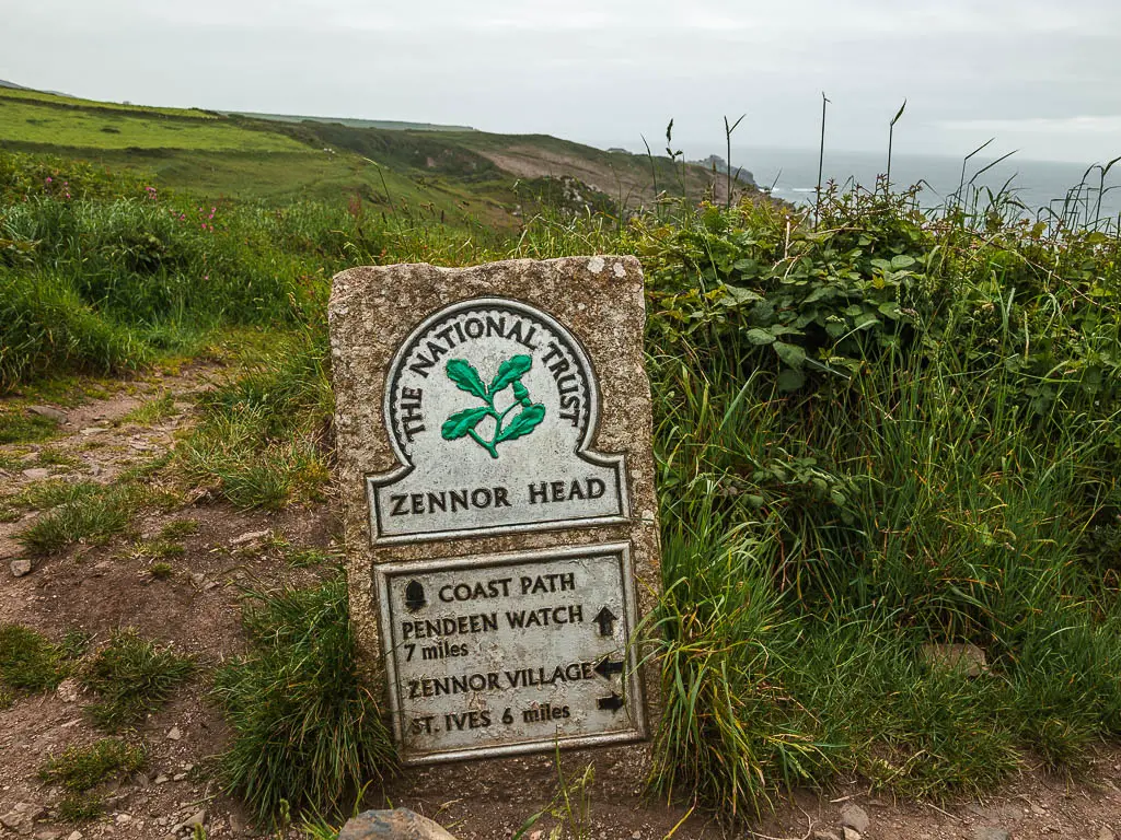 A stone with a plaque saying 'Zennor Head' with an arrow pointing ahead to the coast path, right to walk back to St Ives, and left to walk to the village. 