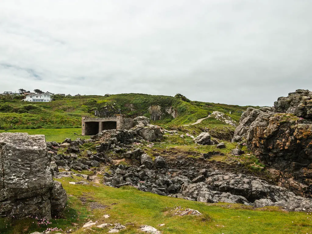 A rugged grassy area, with lots of rocks, and a WWII pill box ahead. 