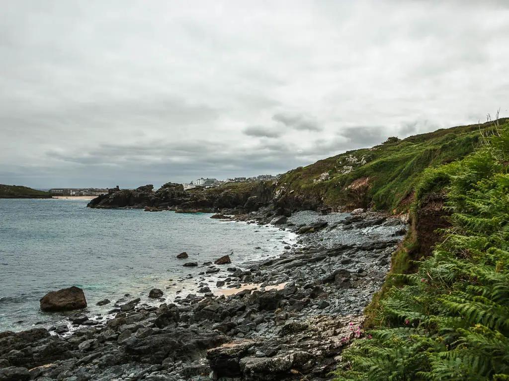 A cove full of black rocks, and enclosed by the grass covered cliffs to the right, on the coast path walk from St Ives to Zennor.