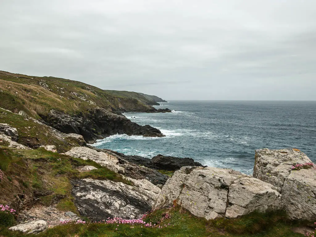 Looking past the large rocks to the rugged coastline ahead, on the coastal St Ives to Zennor walk. The coastline forms numerous coves and peninsula's, and the cliff top is covered in grass. 