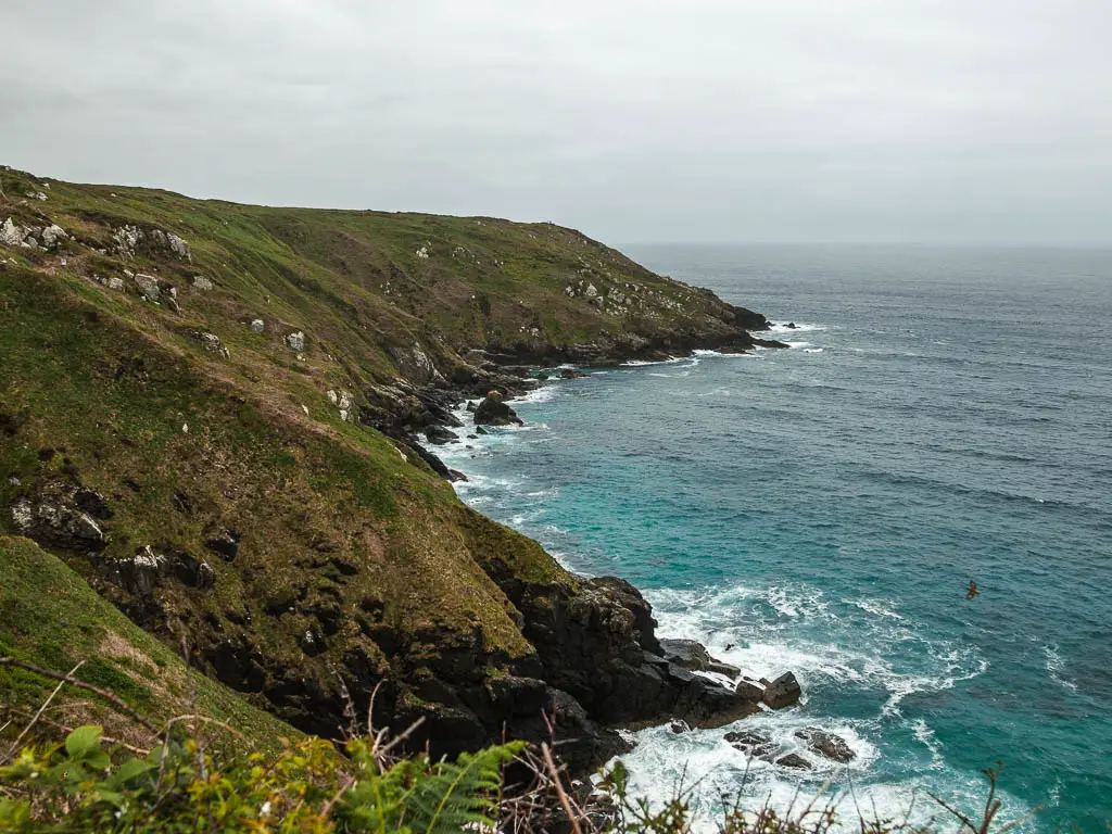 Looking down along the rugged cliffs which slop down to meet the sea, along the coastal St Ives to Zennor walk. The sea is turquoise where it meets the cliffs. 