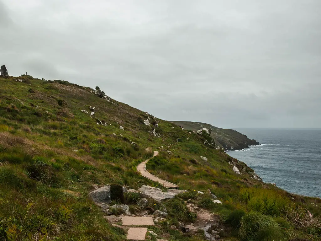 The trail as it goes from rocks to a wooden walkway, snaking across the grass covered clifftop, part way through the St Ives to Zennor walk. 