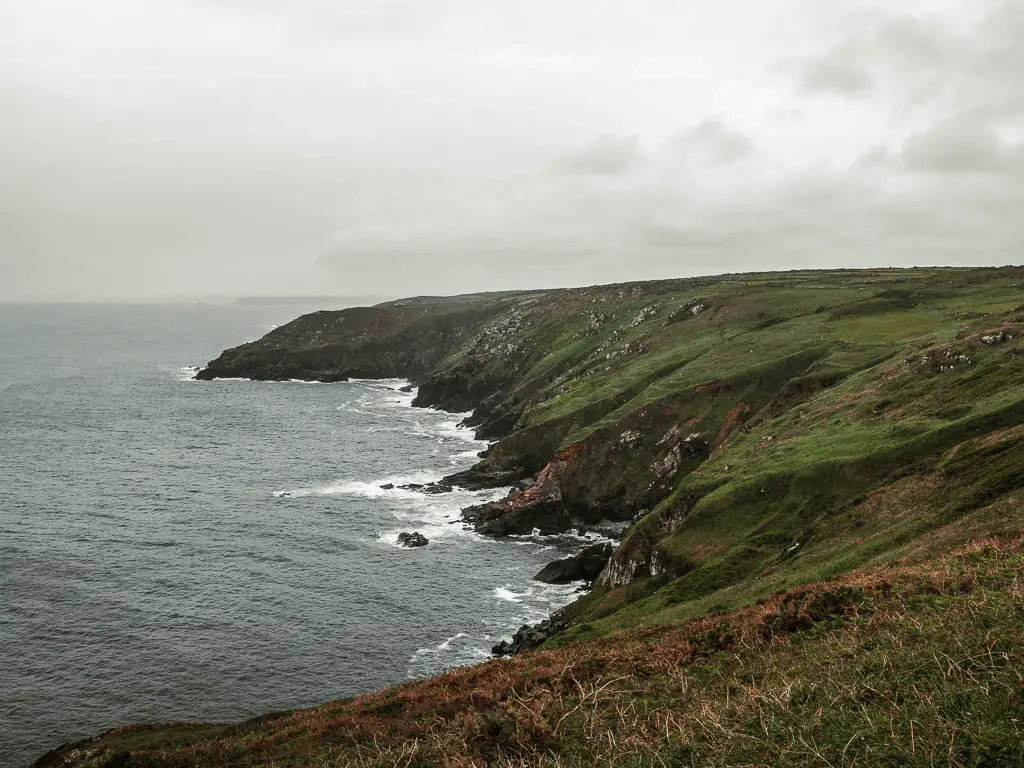 Looking down to the jagged cliff cove on the coastal walk from St Ives to Zennor. The clifftop is covered in grass and slopes down to meet the sea. 