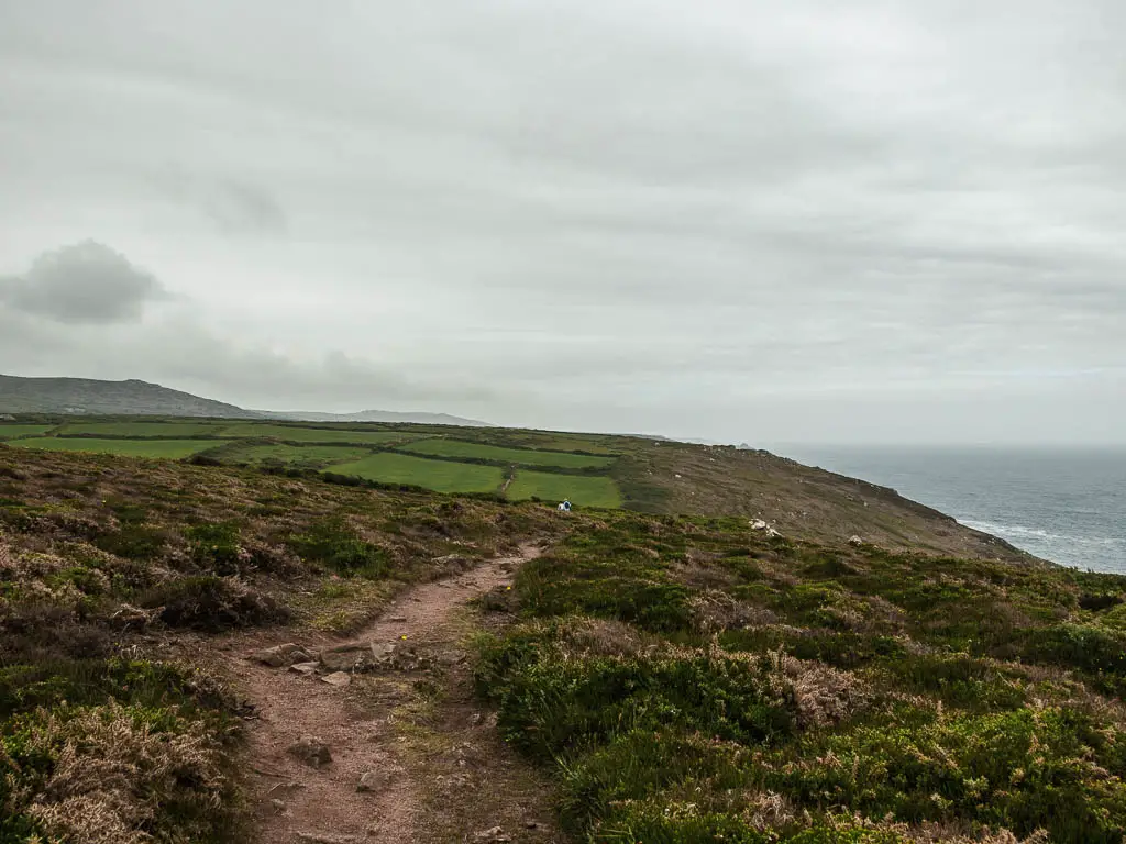 A dirt traill running along the relatively flat clifftop. There are patchwork type green fields in the distance. 