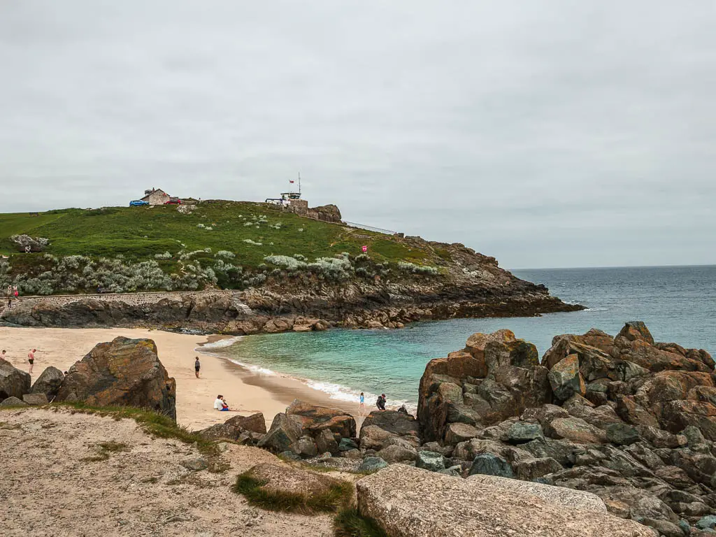 Looking over some rocks tor a sandy beach pillow and a grass covered peninsular hill on the other side, on the walk from St Ives to Zennor. 