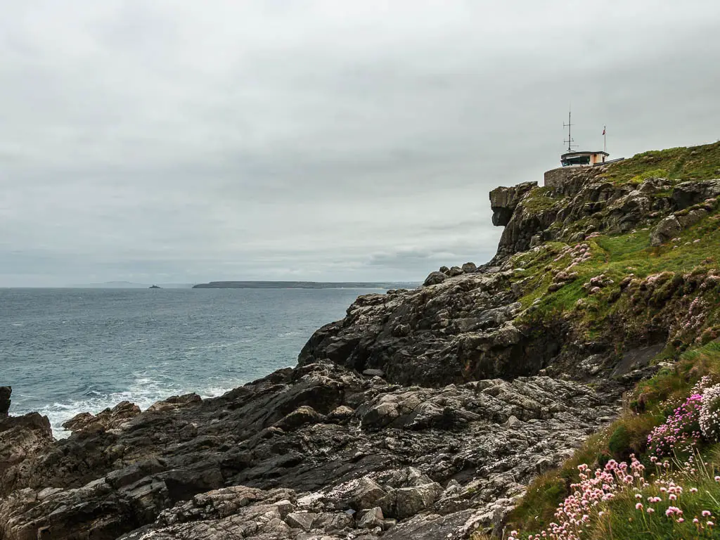 The cliffside as it turns to lots of black rocks with a watchtower at the top, on the coastal walk from St Ives to Zennor.