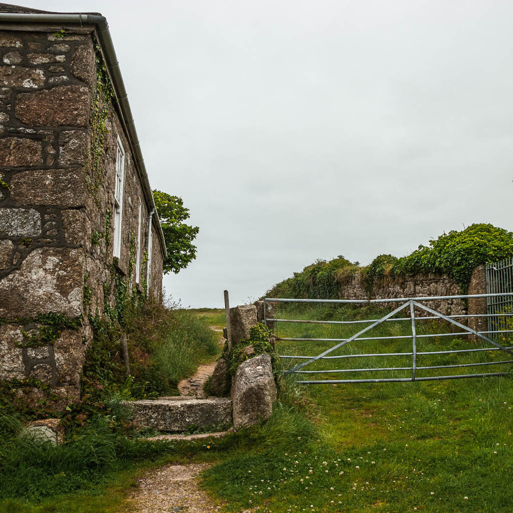 Stone steps leading between a stone house on the left and metal gate on the right.