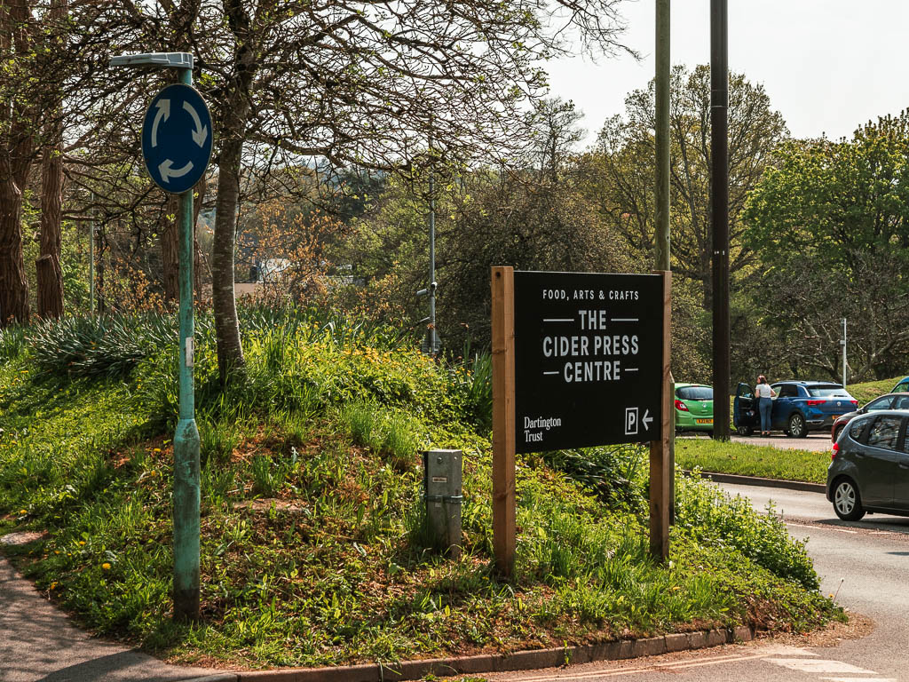 A large black sign saying Cider Press centre on the corner, with some cars on the main road to the right.