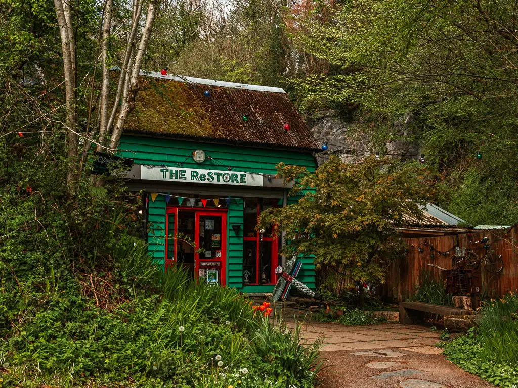 A green painted wooden walled shop nestled in the trees on the Totnes to Dartington circular walk.