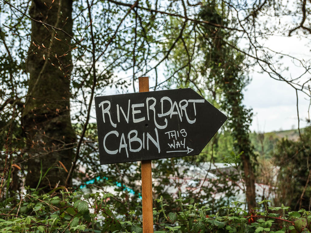 A black arrow signpost pointing to the river dart cabin on the Totnes to Dartington circular walk.