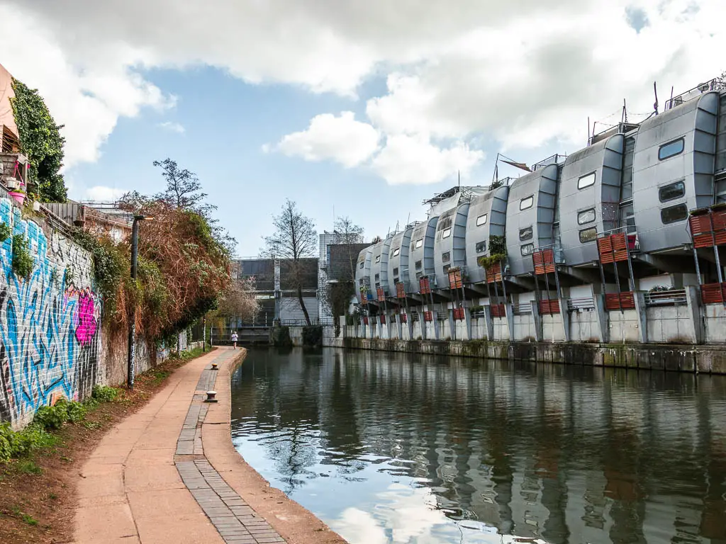 The regents canal path, with a graffiti covered brick wall on the left and spaceship looking apartment buildings on the right.