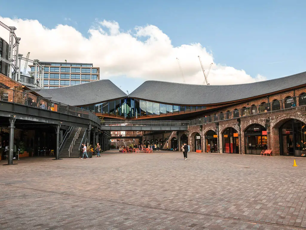 A large empty courtyard surround by shops under brick archways.