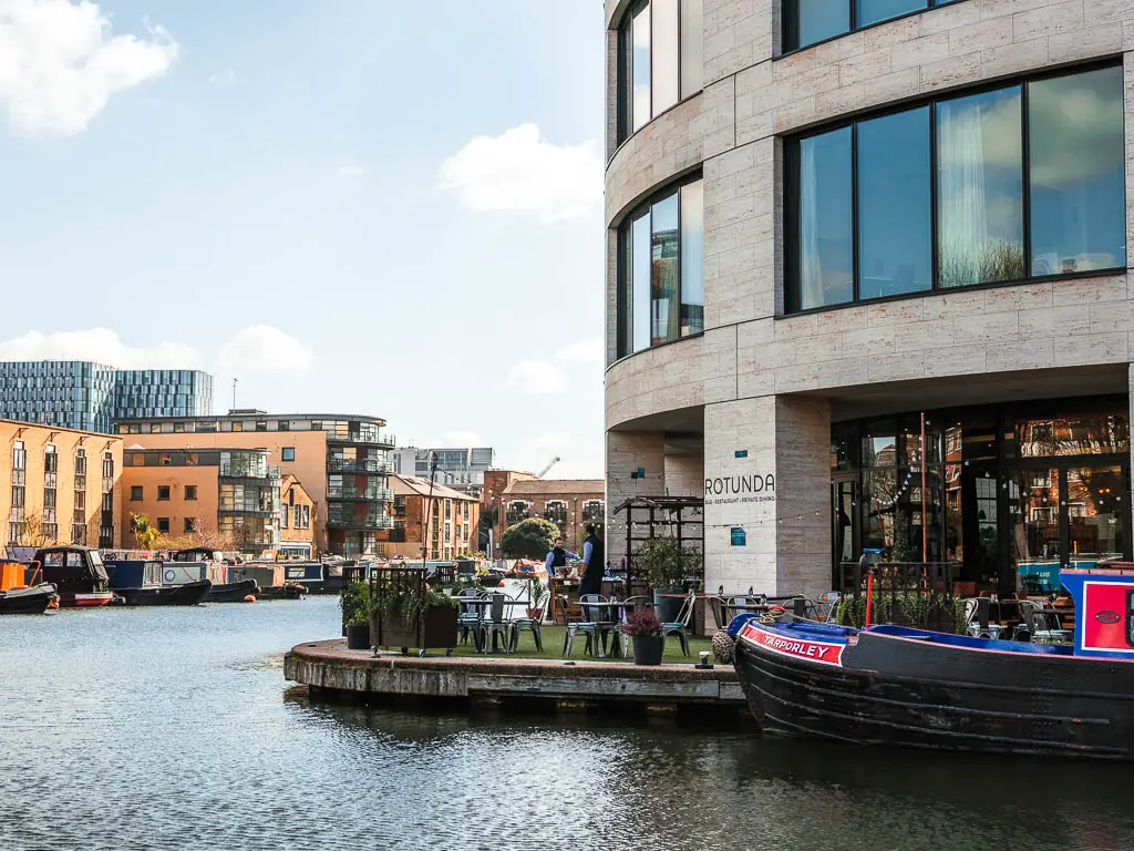 A large cylindrical shaped apartment building on the other side of the canal, with a barge boat moored outside, and terrace restaurant on the canal. 