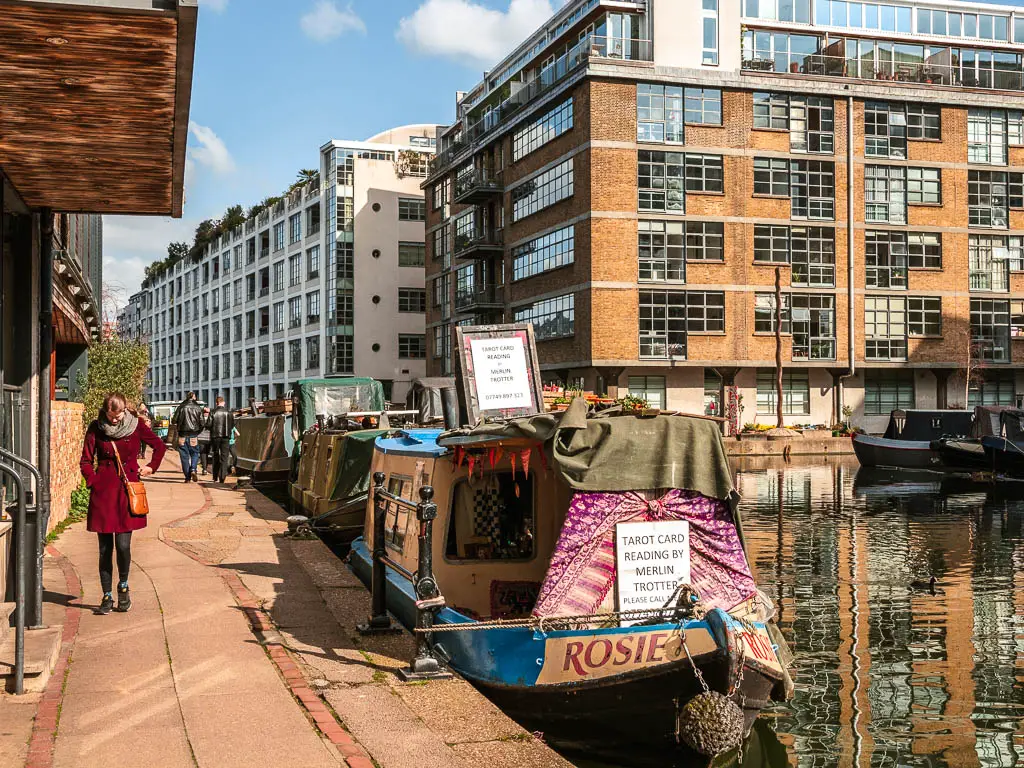 A tarot card reading barge moored to the path on the walk along the Regents Canal in London. There is a woman in a red coat walking along the path. 