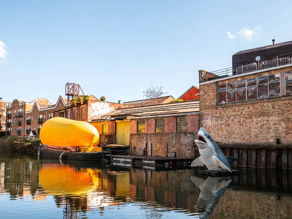 Brick walls of buildings on the other side of the canal, and a big shark statue poking out of the water.