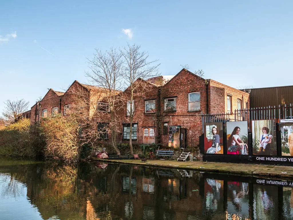 Looking across the canal to an old brick buildings and some artwork posters on the railings.