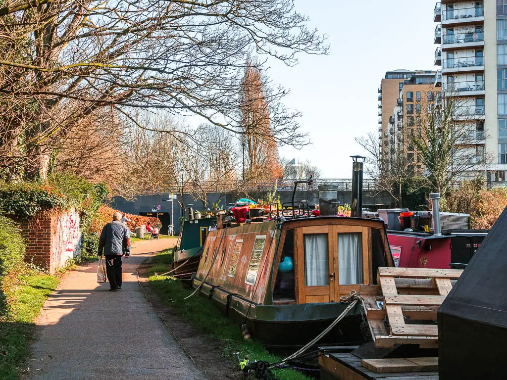 The path on the left with barges moored on the right, and a bit of the Canada Square one building poking up in the distance. 