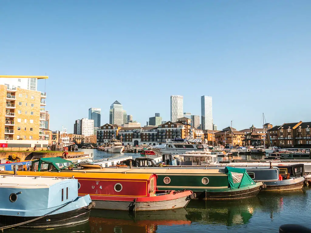 Looking across the water of Limhouse basin with lots of colourful barges and the Canary Wharf skyscrapers in the distance.