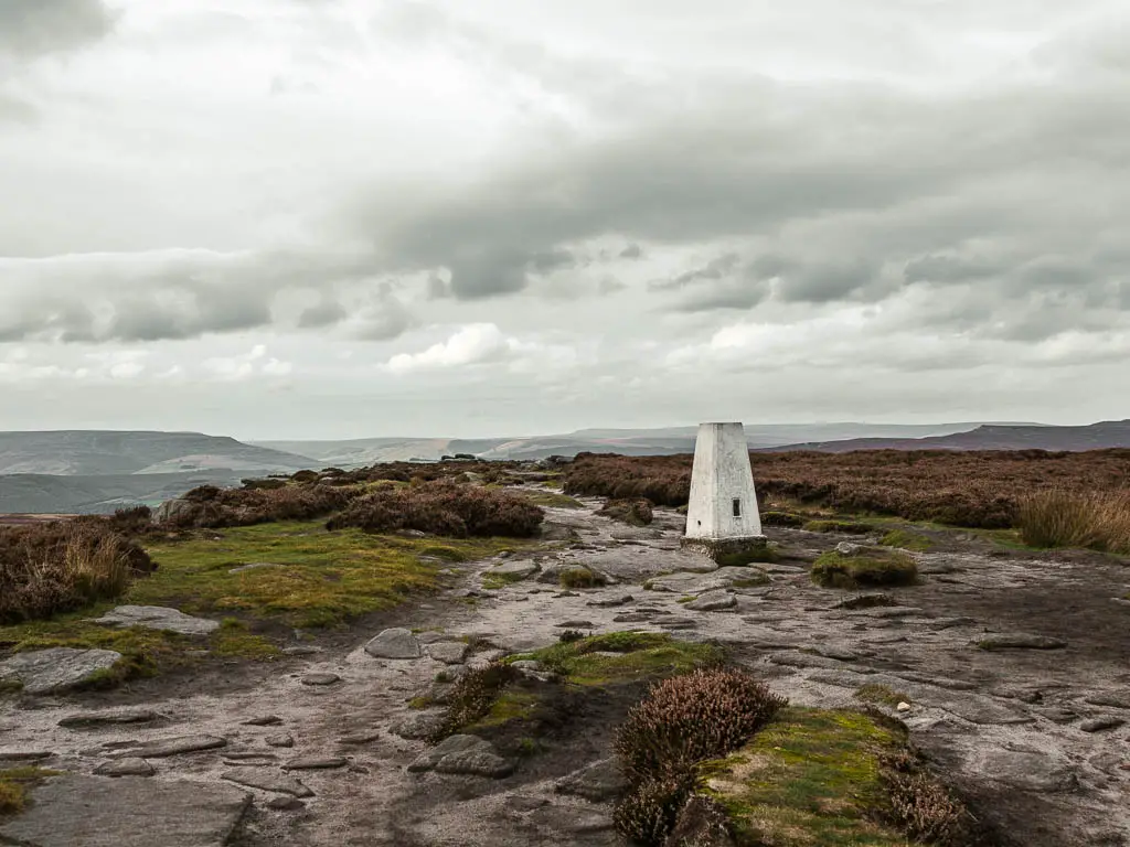 The dirt ground with slabs of rock and a white trig point.