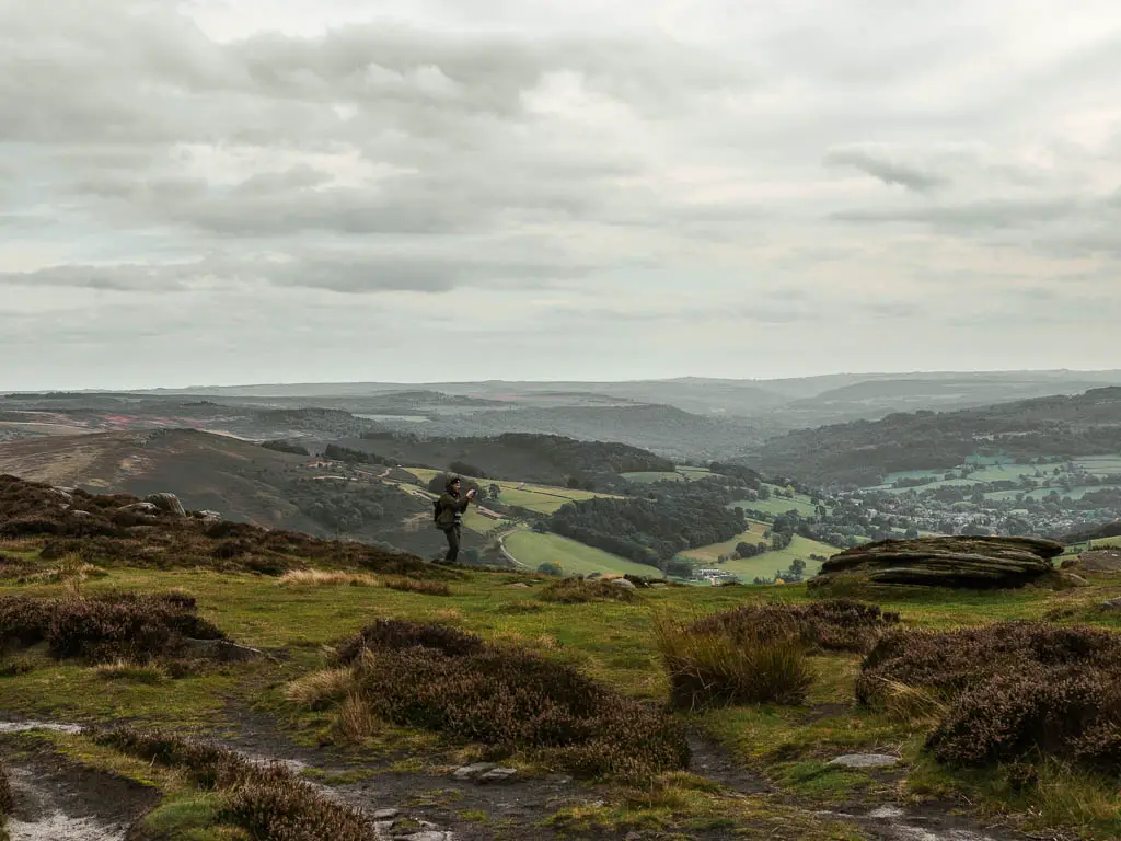 A man standing looking out in the distance to the green undulating hills of the Peak District National Park.