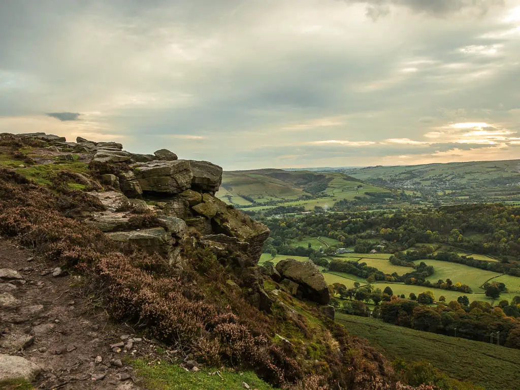 Looking along the side of the rocky cliff face on the circular Bamford Edge walk, with a view to the green valley below to the right.