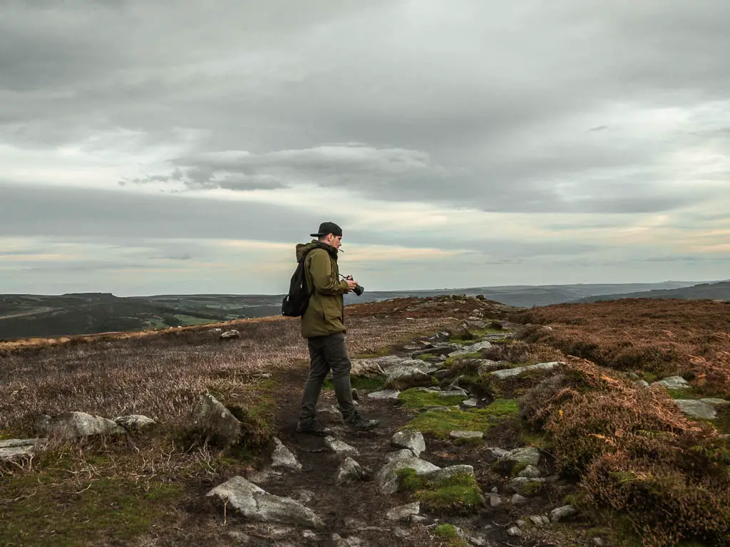 A man standing on a rocky dirt path, holding a camera.