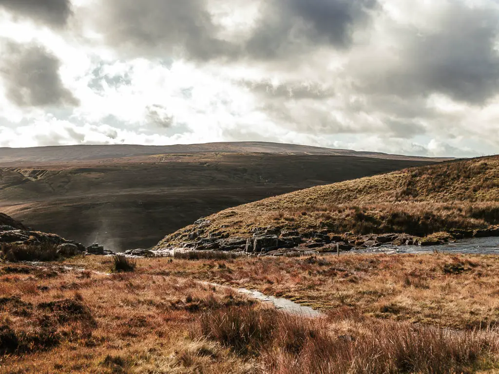 Looking across the hay coloured grass as it leads to a drop, with mist rising up along the Cauldron Snout walk.