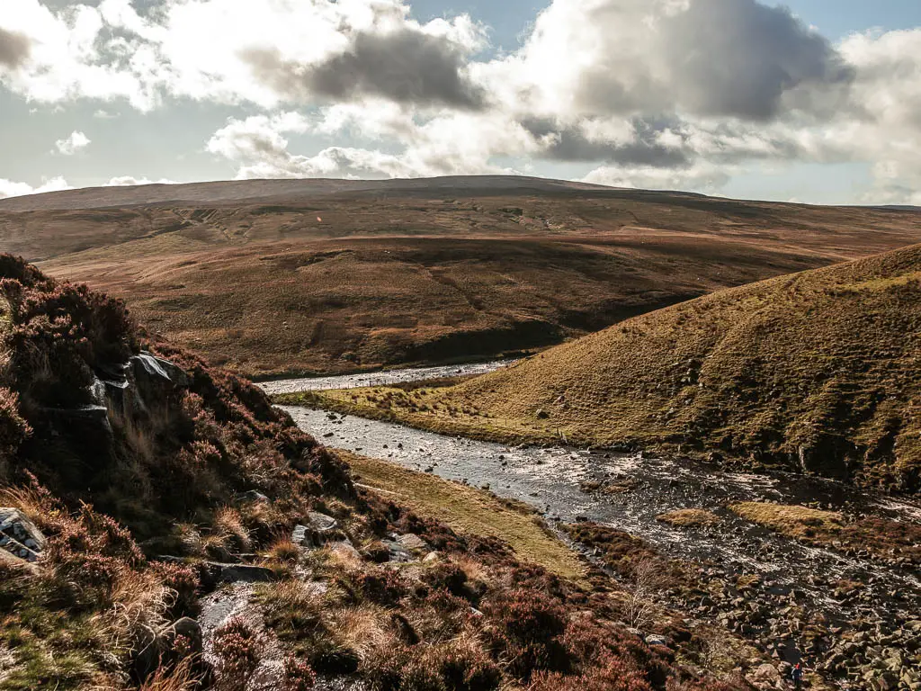 The rover flowing through the valley, with a rocky hill on the left, and grass hills ahead and on the right.