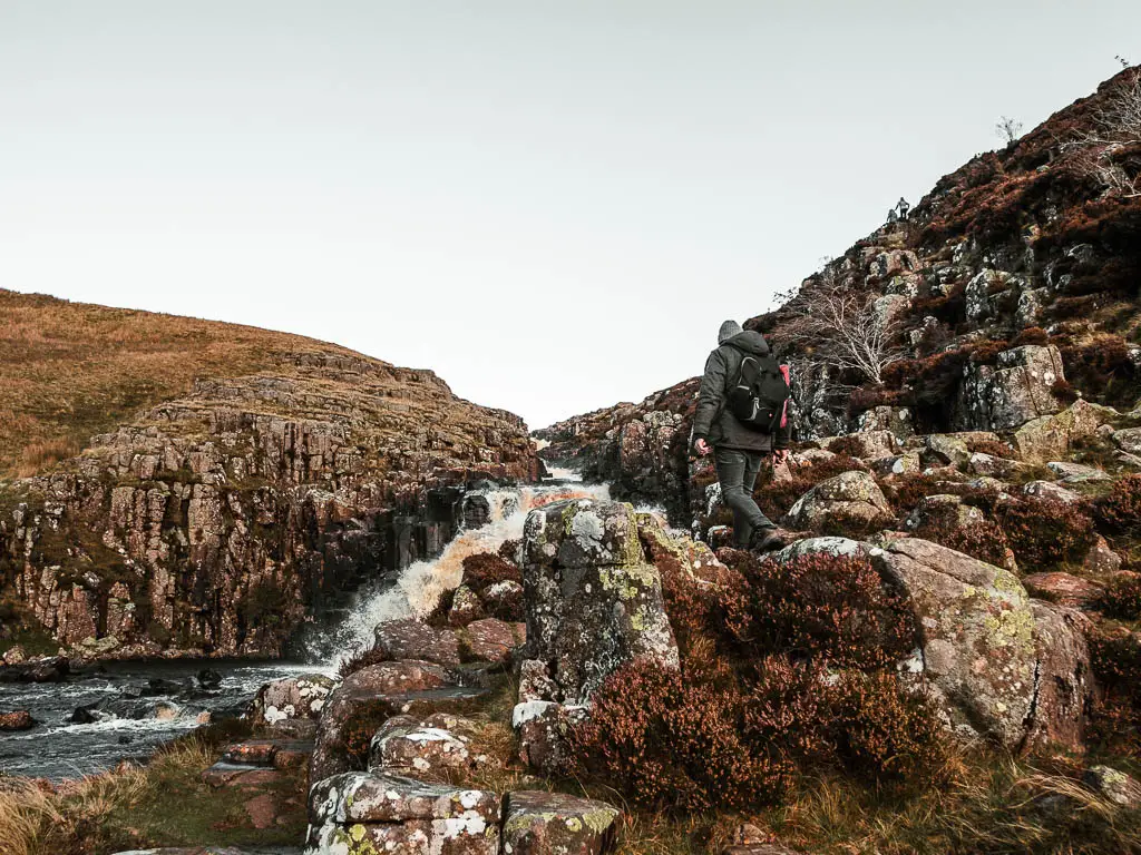 Lots of big rocks partially covering the water crashing down at Cauldron snout, with a man walking across the rocks.