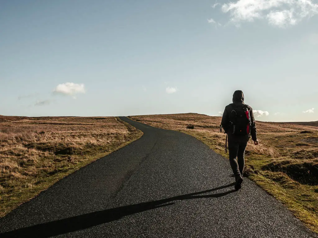 A man walking on a long black tarmac road.