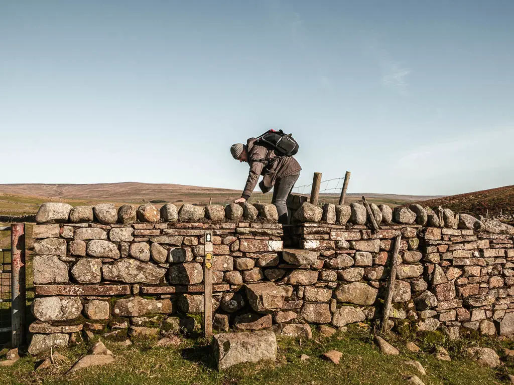 A man climbing over a stone wall with stone steps.