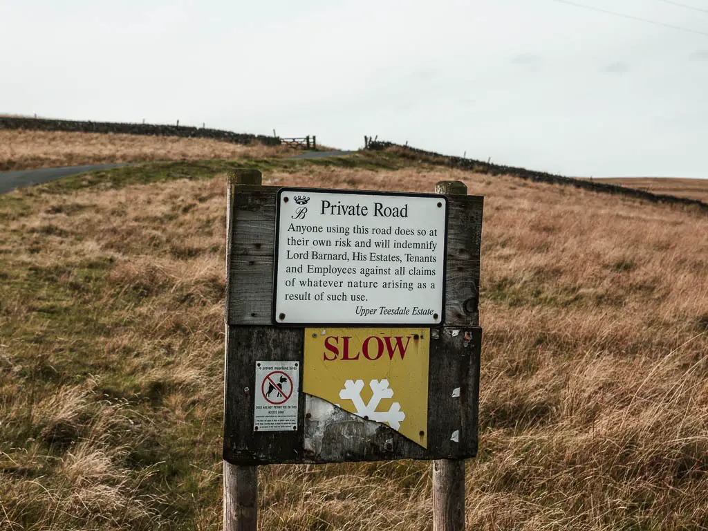 A sign in front of a tall grass field. The sign says 'private road'