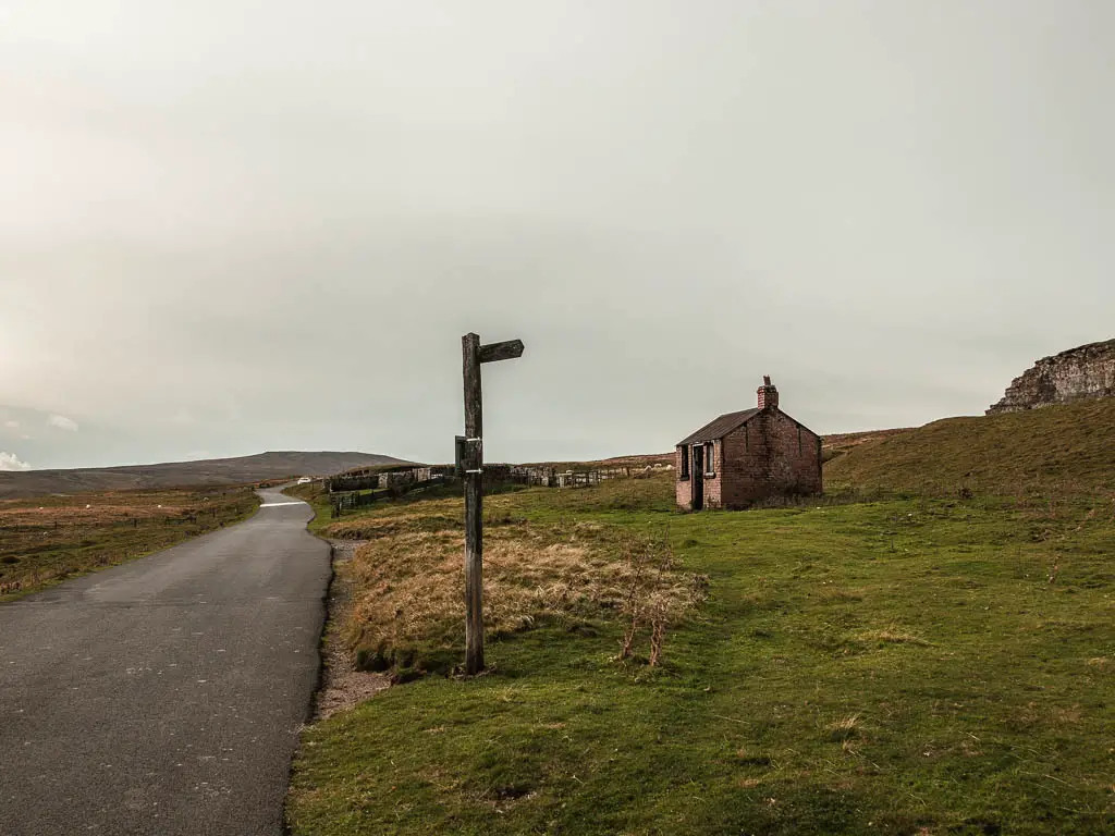 A road on the left, and a small abandoned shed on the grass on the right, at the end of the Cauldron Snout walk. 