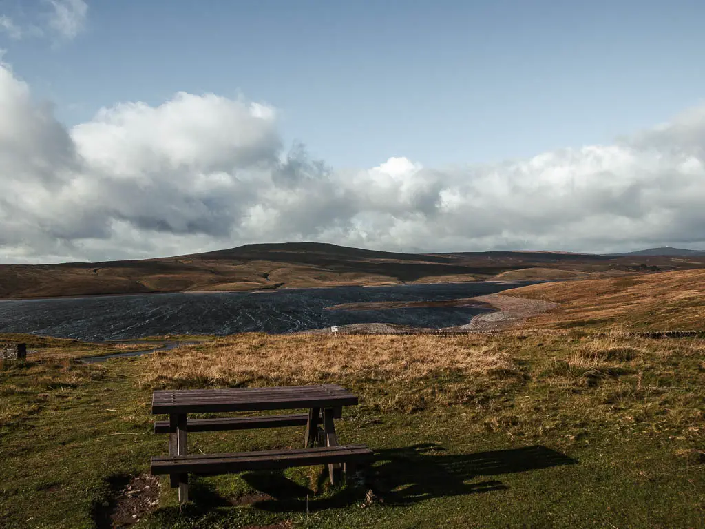 A picnic bench on the grass, with the Cow Green Reservoir ahead, at the start of the walk towards Cauldron snout.