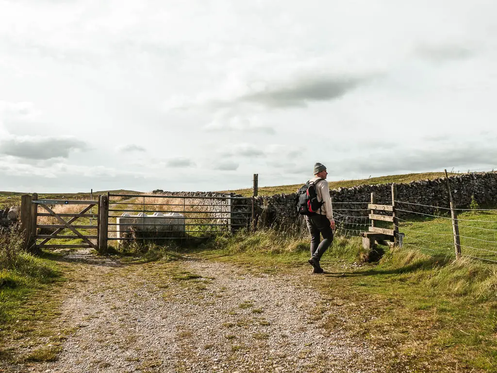 A man waling to a stile on the right side of the gravel path.